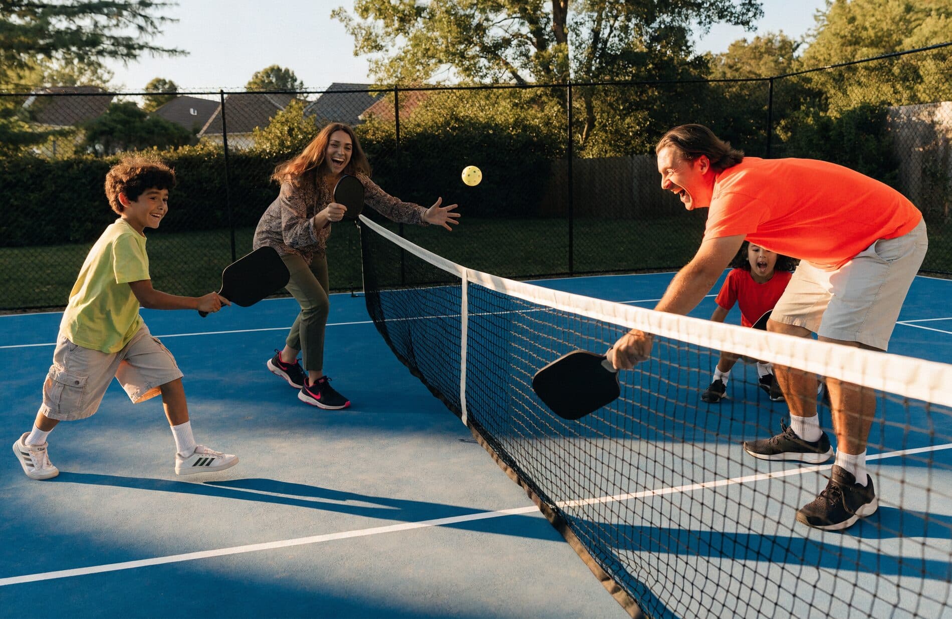 A family plays pickleball on a backyard court at golden hour
